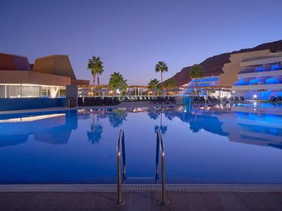 Evening view of a hotel with illuminated pool and palm trees in the background.