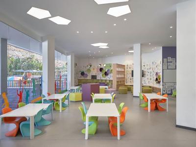 Área de juegos para niños luminosa con sillas y mesas coloridas en una zona de hotel con grandes ventanas.