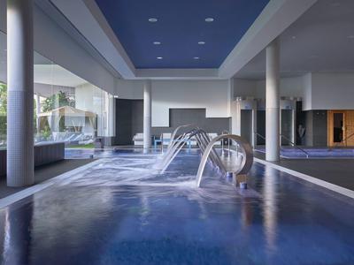 Piscina cubierta moderna con columnas, luz natural y chorros de agua decorativos.