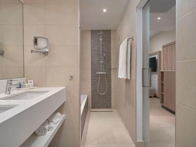 Baño moderno con lavabo claro, ducha, bañera y vista al dormitorio.