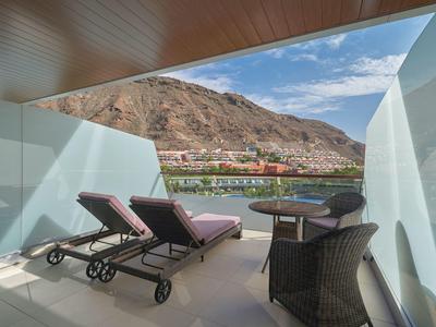 Balcón con tumbonas y sillas, vista a montaña y mar en un hotel.