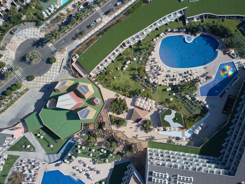 Vista aérea de un hotel con piscina, jardín y áreas de descanso junto a un canal.