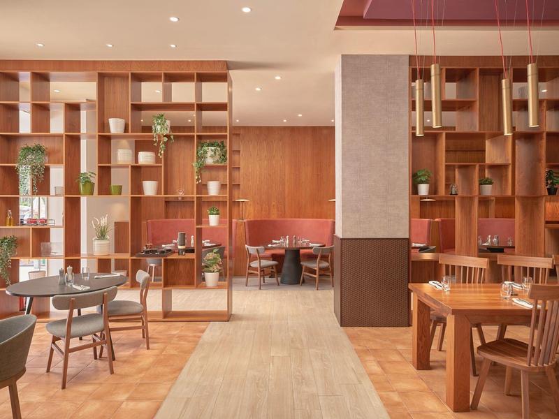 Restaurante moderno y luminoso con muebles de madera, pasillo con alfombra y biombos decorativos.