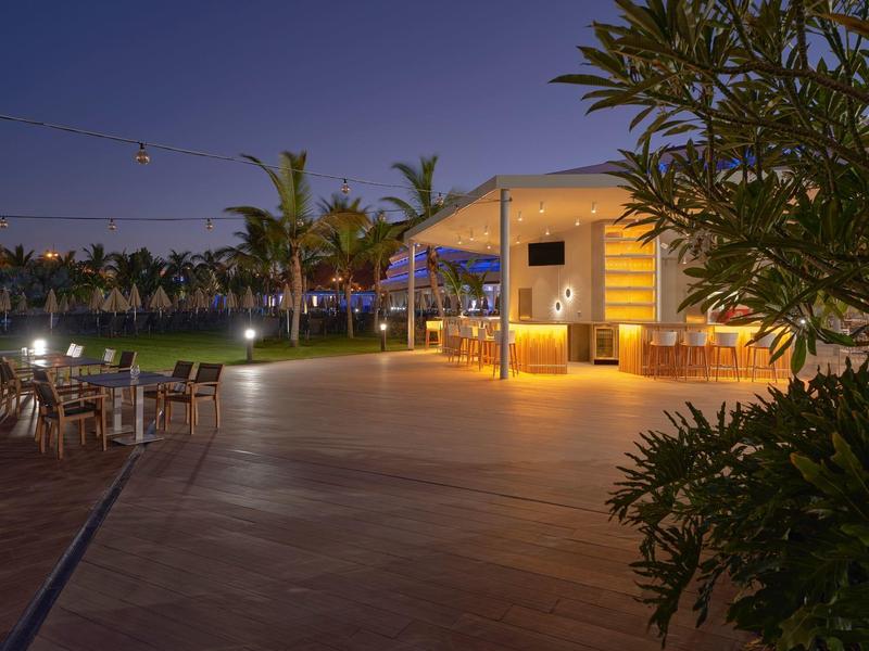 Terraza nocturna de un hotel con iluminación, plantas y mesas al aire libre.