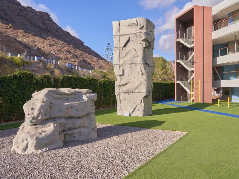 Muro de escalada y bloque de boulder en una zona ajardinada junto a un hotel en la montaña.