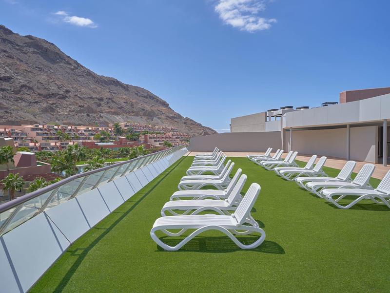 Sillas reclinables en césped con vista a montañas y cielo azul.