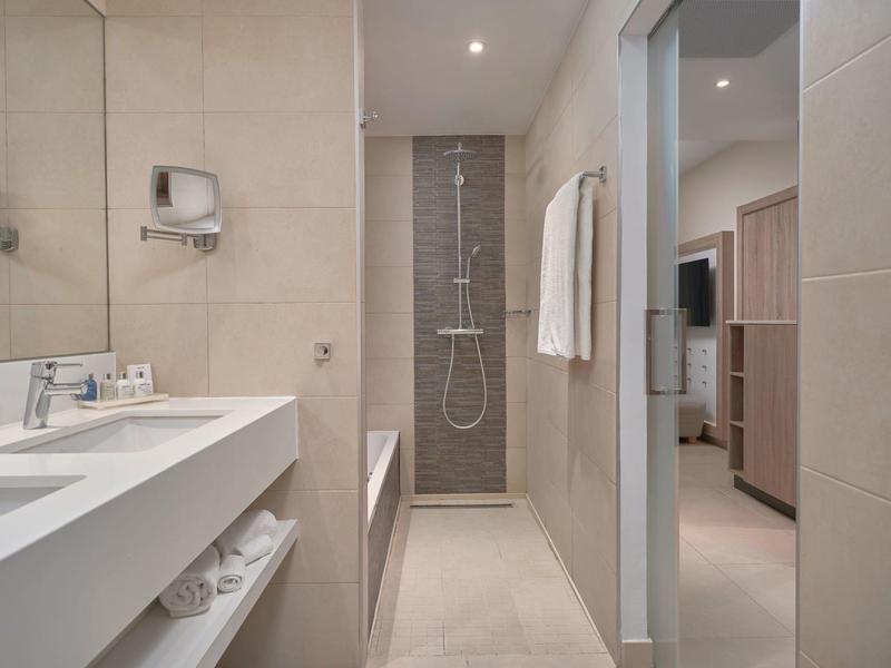 Baño moderno con lavabo claro, ducha, bañera y vista al dormitorio.