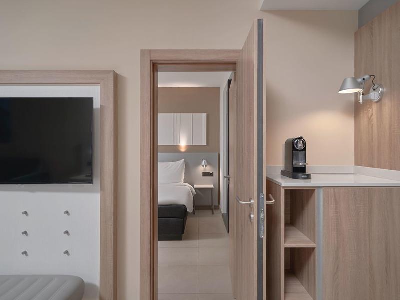 Habitación de hotel con marco de puerta abierto, vista al dormitorio con cama y lámpara de noche.