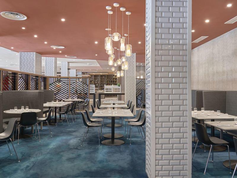 Comedor moderno con mesas blancas, sillas y lámparas colgantes en un ambiente relajado.