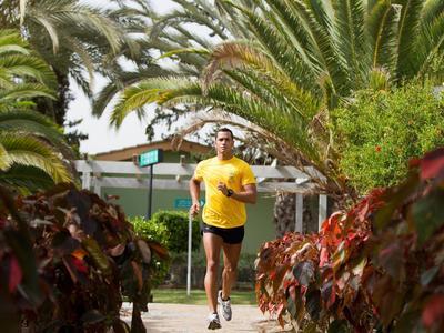 Homme courant sur un chemin bordé de palmiers et de plantes colorées.