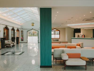 Hall d'hôtel moderne avec des fauteuils blancs, des coussins orange et des colonnes vertes.