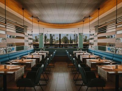 Restaurant moderne avec des sièges verts foncés et de grandes fenêtres donnant sur des palmiers.