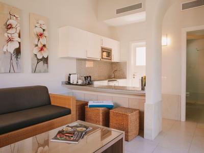 Salon d'hôtel confortable avec canapé, œuvres d'art, kitchenette et poufs.