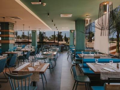 Restaurant moderne avec chaises et tables bleues, grandes fenêtres offrant vue sur des palmiers.