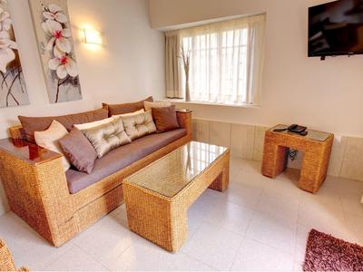 Coin salon confortable avec meubles en rotin, table basse en verre et art mural décoratif.