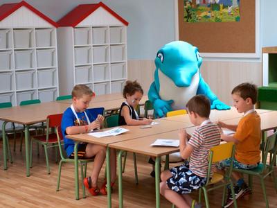 Des enfants sont assis à une table dans une classe avec une personne en costume de dauphin.