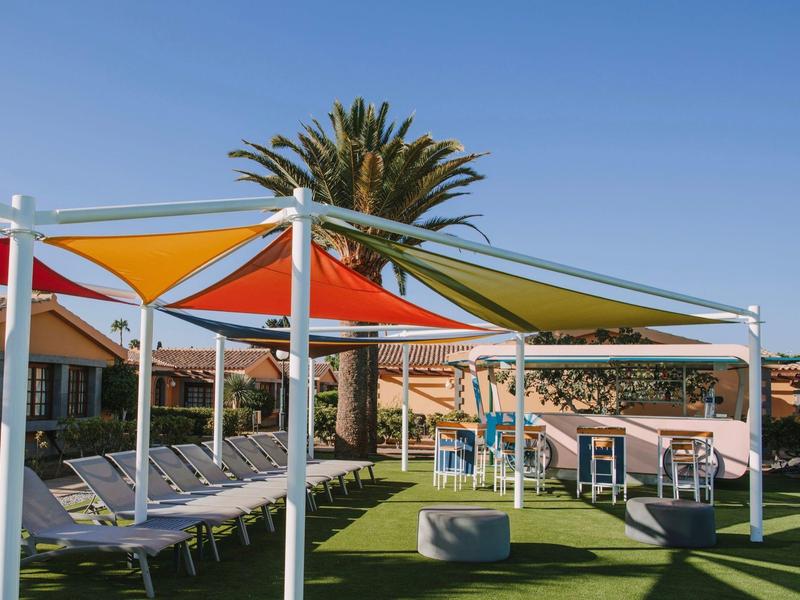 Voiles d'ombrage colorées au-dessus de chaises longues et tables près d'un bâtiment d'hôtel