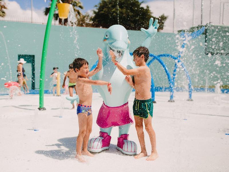 Deux garçons tapent dans la main d'un dauphin bleu dans une aire de jeu aquatique.