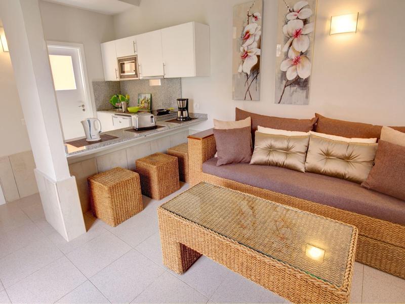 Salon d'hôtel confortable avec canapé, coussins, table basse et kitchenette.