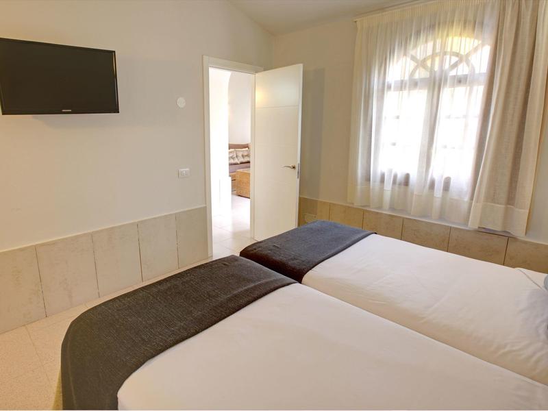 Chambre d'hôtel lumineuse avec deux lits simples, fenêtre avec rideaux et télévision murale.