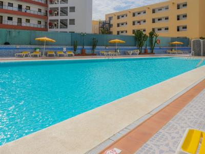 Gran piscina exterior con sombrillas y tumbonas junto a edificios de varios pisos.