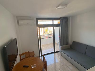 Habitación pequeña de hotel con mesa de comedor, sillas, sofá y balcón con ventanas de cristal.