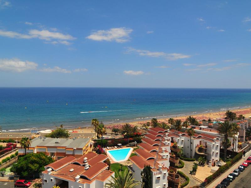 Vista aérea de un hotel junto al mar con piscina y una larga playa bajo un cielo azul.