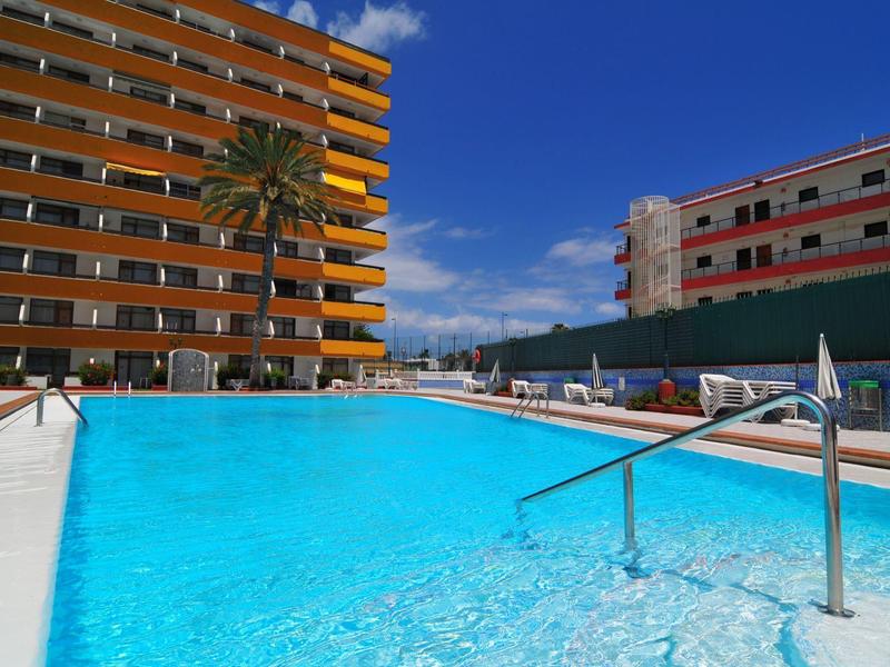 Gran piscina exterior con pasamanos, rodeada de hoteles de varios pisos bajo un cielo despejado.