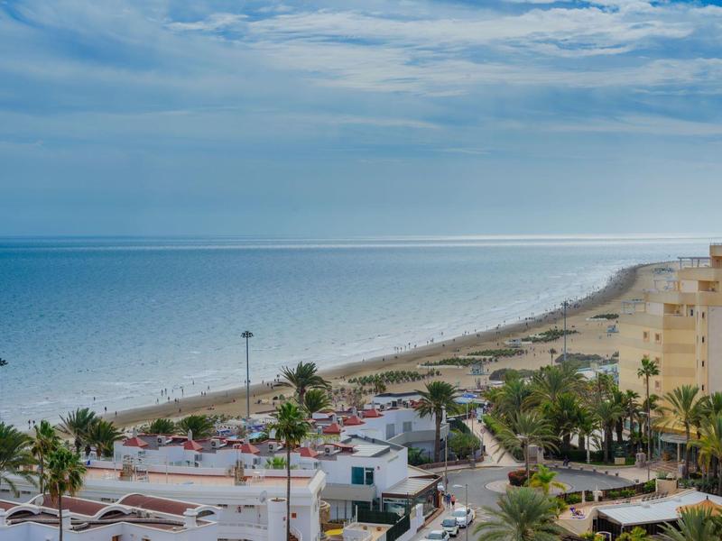 Vista de una ciudad costera con playa, mar y cielo parcialmente nublado.