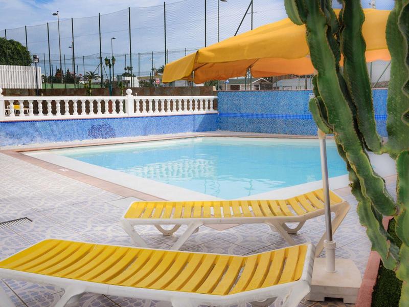 Piscina vacía con tumbonas amarillas y sombrilla en un día soleado.