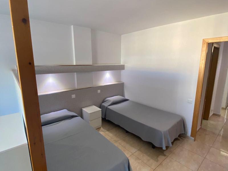 Habitación de hotel sencilla con dos camas individuales y cubrecamas grises, suelo de baldosas claras.
