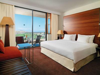 Helles Hotelzimmer mit großem Doppelbett, Holzschrank, rotem Sofa und Balkon mit Meerblick.