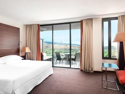 Geräumiges Hotelzimmer mit großem Bett, Balkon mit Meerblick, roten Sesseln und Holzvertäfelung.