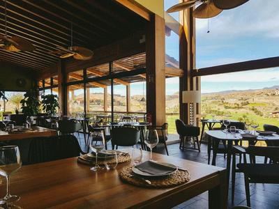 Gemütliches Restaurant mit Holztischen, schwarzen Stühlen und weitem Fensterblick auf grüne Landschaft.