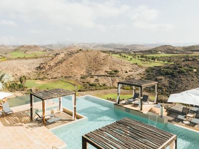 Luxuriöser Poolbereich mit Liegen, weißen Sonnenschirmen und weitem Blick auf hügelige Landschaft.