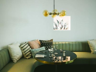 Elegante Sitzecke mit grünem Polstersofa, runden schwarzen Tisch und goldgelber Hängeleuchte.