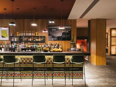 Espace bar d'hôtel moderne avec tabourets, éclairage et sélection de spiritueux.