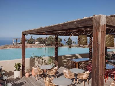 Terrasse d'hôtel avec tables et chaises sous pergola en bois près de la piscine et vue sur l'océan.