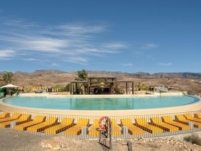 Piscine ronde avec chaises longues jaunes et paysage désertique en arrière-plan.