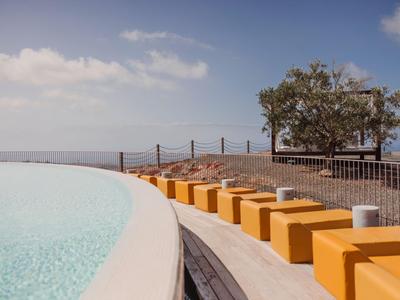 Piscine moderne avec sièges cubes jaunes et vue sur la mer sous un ciel bleu.