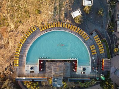 Piscine extérieure semi-circulaire avec chaises longues jaunes et terrasse en bois centrale dans une zone d'hôtel.