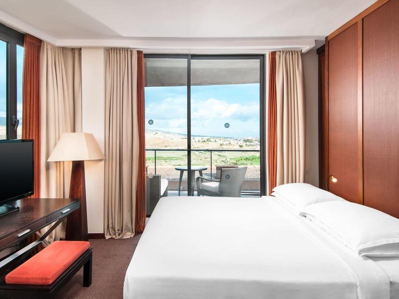 Schlafzimmer mit großem Bett, TV, Stehlampe und Balkon mit Aussicht bei Tageslicht.