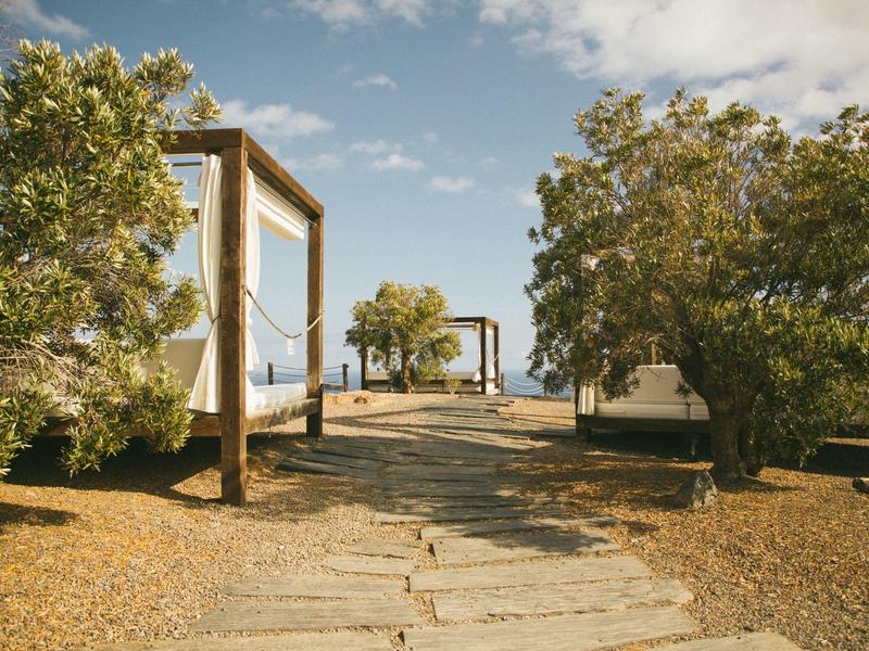 Wanderweg mit Holzstegen und Sitzgruppen, umgeben von Büschen unter blauem Himmel.