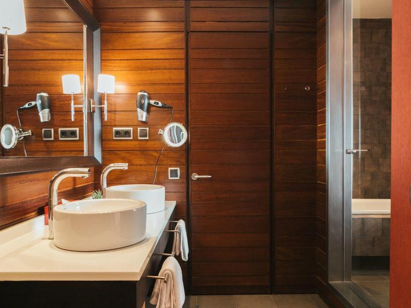 Modernes Badezimmer mit rundem Waschbecken, Holzverkleidung und Glasdusche in warmen Farben.