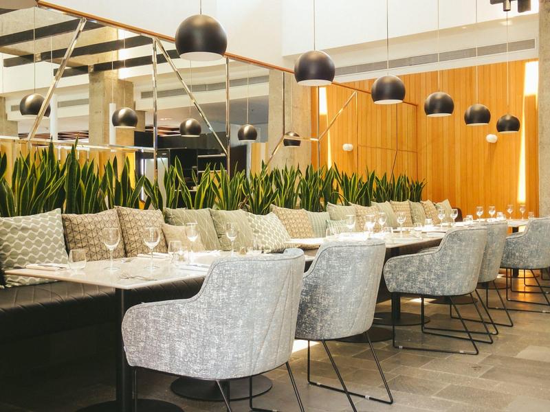 Modernes Restaurant mit grauen Polstersesseln, Holzvertäfelung und grünen Pflanzen als Dekor.