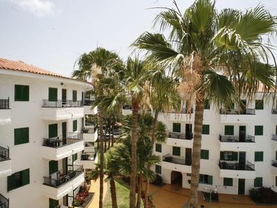 Cortile di un hotel con edifici bianchi, balconi e alte palme sotto un cielo nuvoloso.