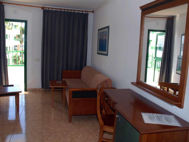 Hell eingerichtetes Wohnzimmer mit Sofa, Holzmöbeln, großem Spiegel und offenem Balkon.