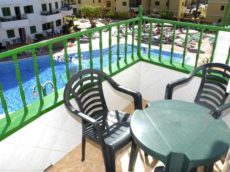 Balkon mit grünem Metallgeländer, drei schwarzen Plastikstühlen und grünem Tisch, Blick auf Pool.