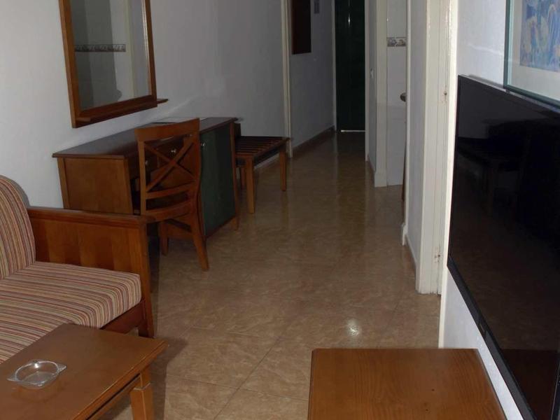 Schmaler Flur mit beige Fliesen, braunen Holzmöbeln, Sofa und Fernseher an der Wand.