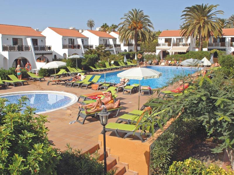 Hotelcomplex met zwembad, ligstoelen en meerlaagse gebouwen met rode daken.